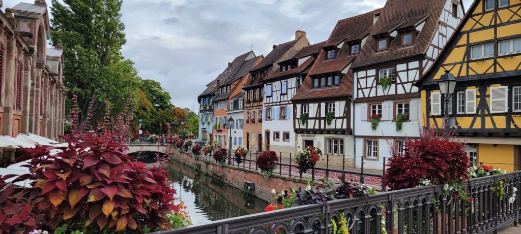 Strasbourg, France photo from a bridge over a small river running between quaint half-timber buildings.