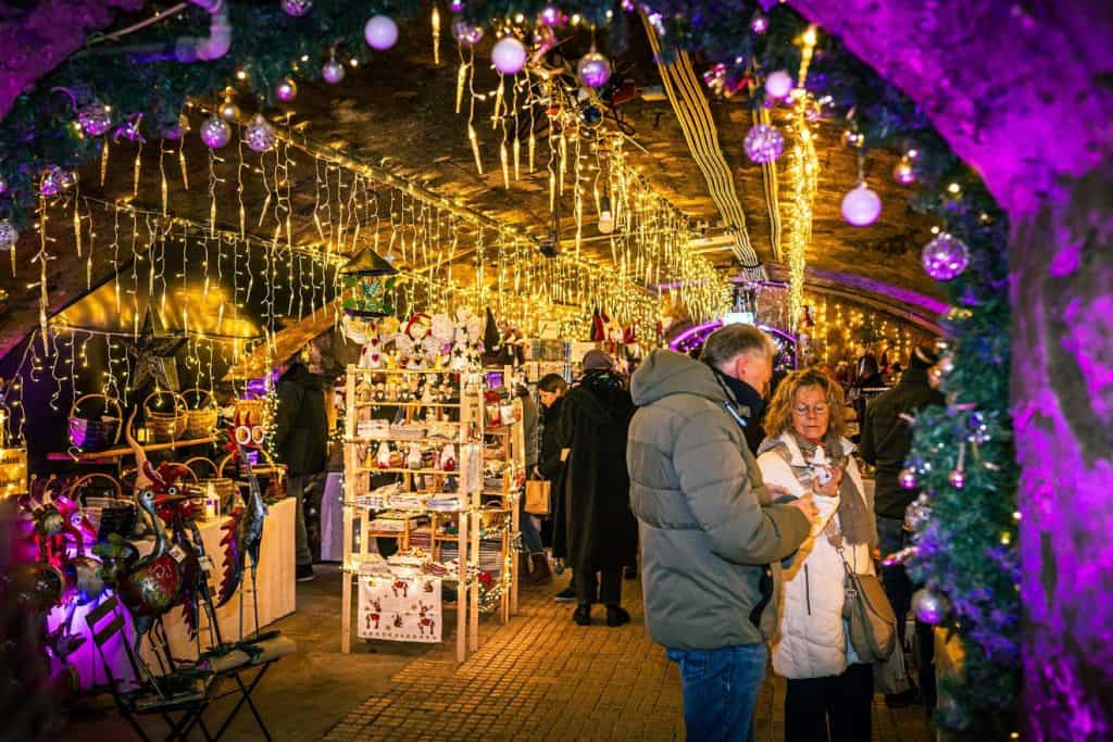 Shoppers browsing a Christmas market set inside a lit-up historic wine cellar