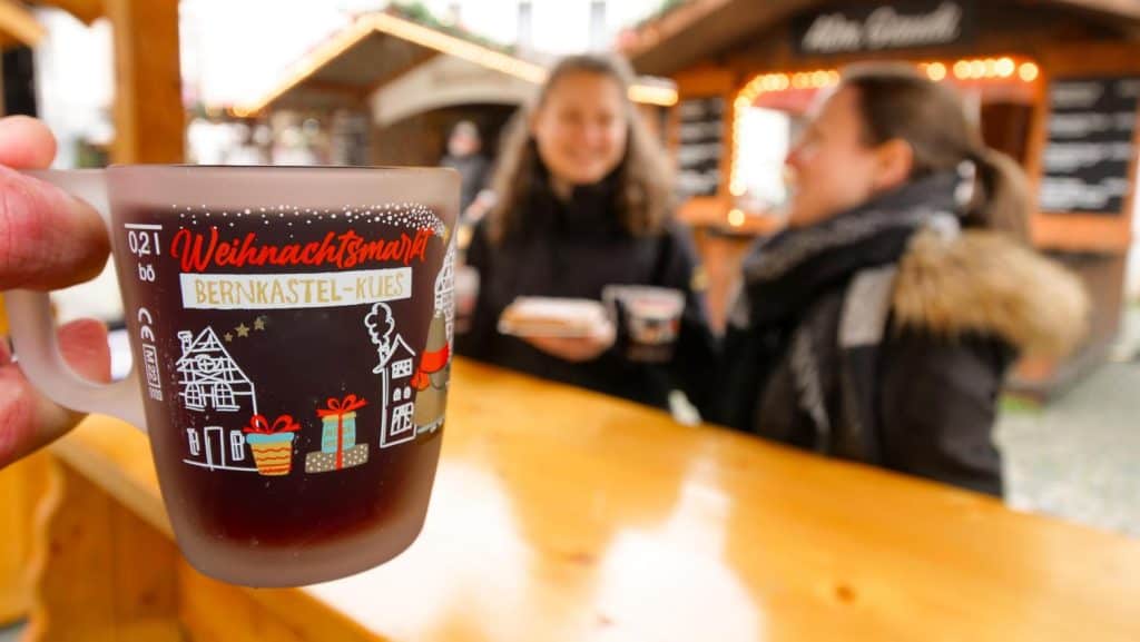 Friends sharing mulled wine in souvenir mugs at a German Christmas market